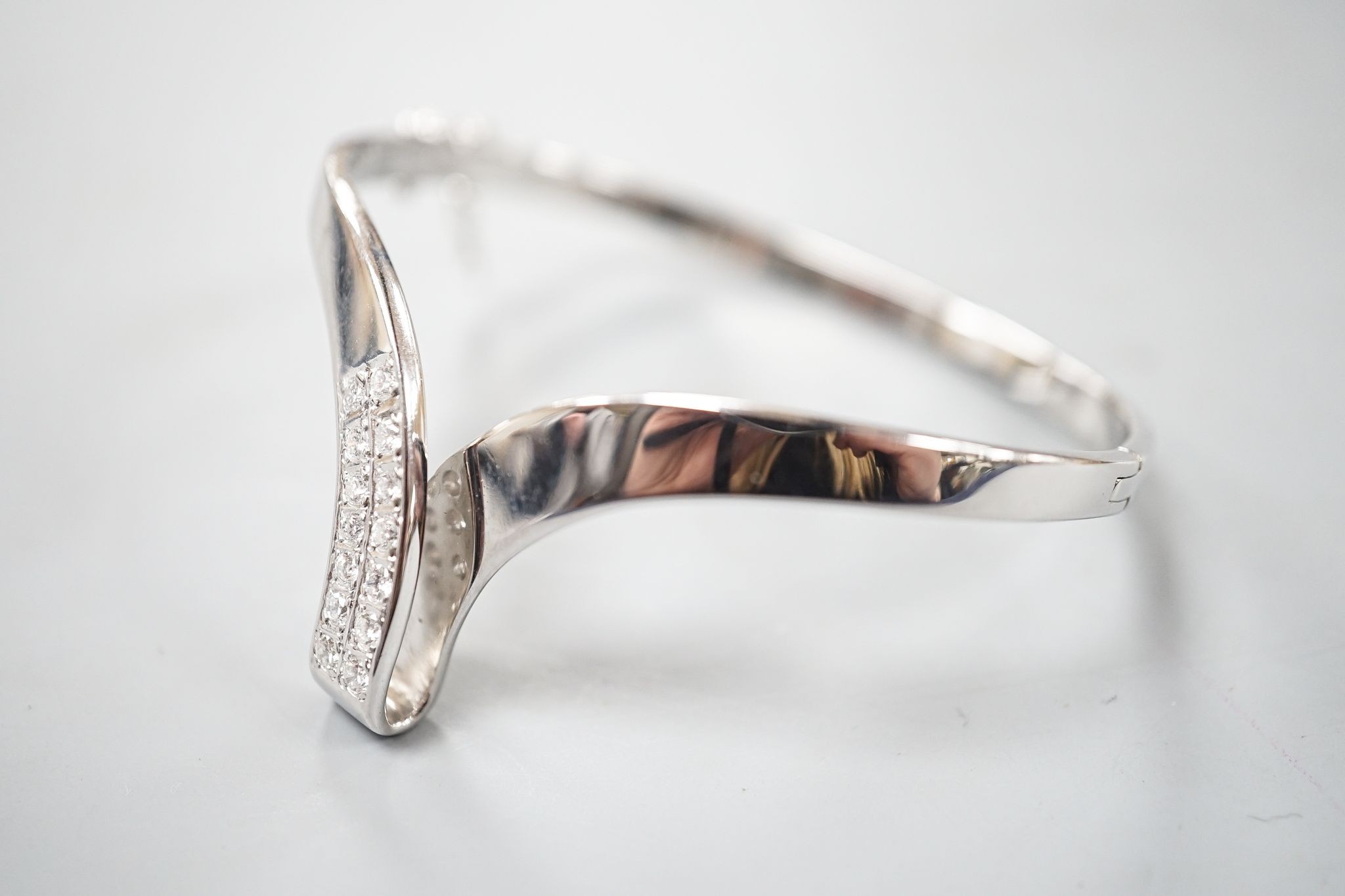 A modern 585 white metal and twelve stone diamond set wishbone shaped hinged bangle, gross 19.7 grams.